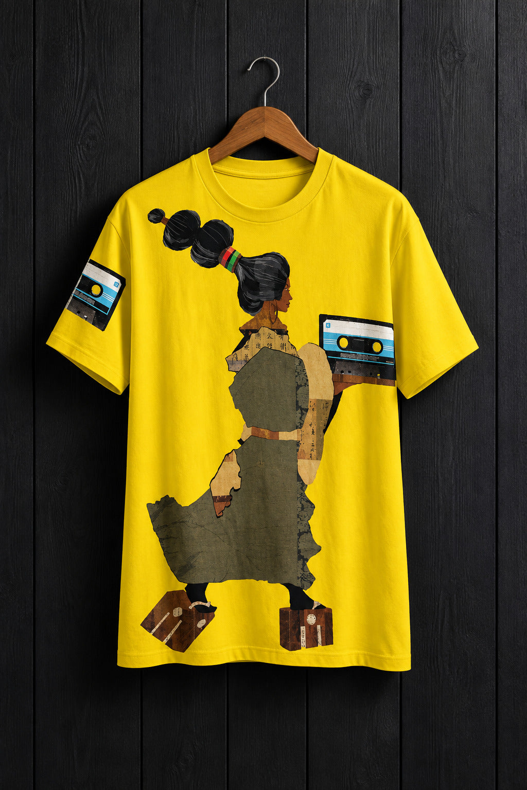 A bright yellow short-sleeve t-shirt hanging on a wooden hanger against a light gray wall. The shirt features a graphic illustration of a woman with high black hair holding cassette tapes, with cassette tape graphics on the sleeves and a small signature 'BAGANA' near the bottom right.