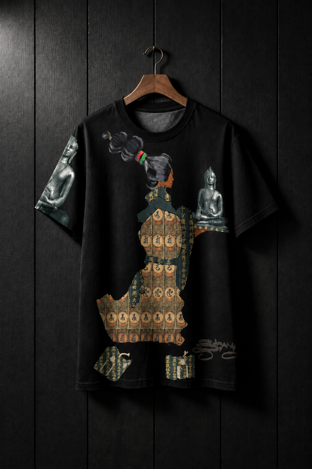 A black short-sleeve t-shirt hanging on a wooden hanger against a plain white wall. The shirt features a large graphic print depicting a woman in traditional patterned clothing with Buddha statues on both sides.
